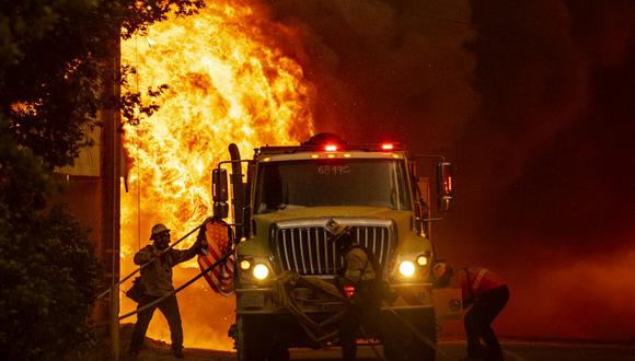 Un bombero salva una bandera estadounidense mientras las llamas consumen una casa durante el incendio de Dixie en Greenville, California, el 4 de agosto de 2021 (Foto de Josh Edelson / AFP).