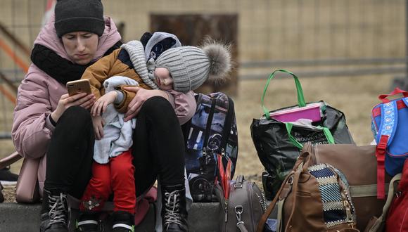 Una mujer con su hijo revisa su teléfono móvil mientras espera la reubicación fuera del principal refugio y centro de reubicación en Przemysl, sureste de Polonia, el 16 de marzo de 2022. (Foto: Louisa GOULIAMAKI / AFP)