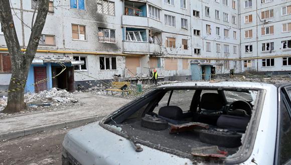 Una imagen muestra un automóvil dañado mientras los trabajadores de los servicios comunales tapan los agujeros en las paredes y las ventanas rotas en un edificio residencial dañado por los bombardeos, en Kharkiv, el 14 de abril de 2022, en medio de la invasión rusa lanzada contra Ucrania. (Foto de SERGEY BOBOK / AFP)