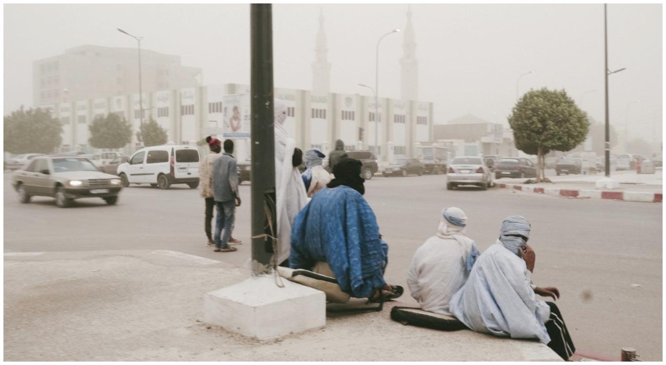 Los hombres se sientan en la calle en Nouakchott el 24 de febrero de 2020 cuando una gran tormenta de arena llega a Mauritania. (Foto: AFP)