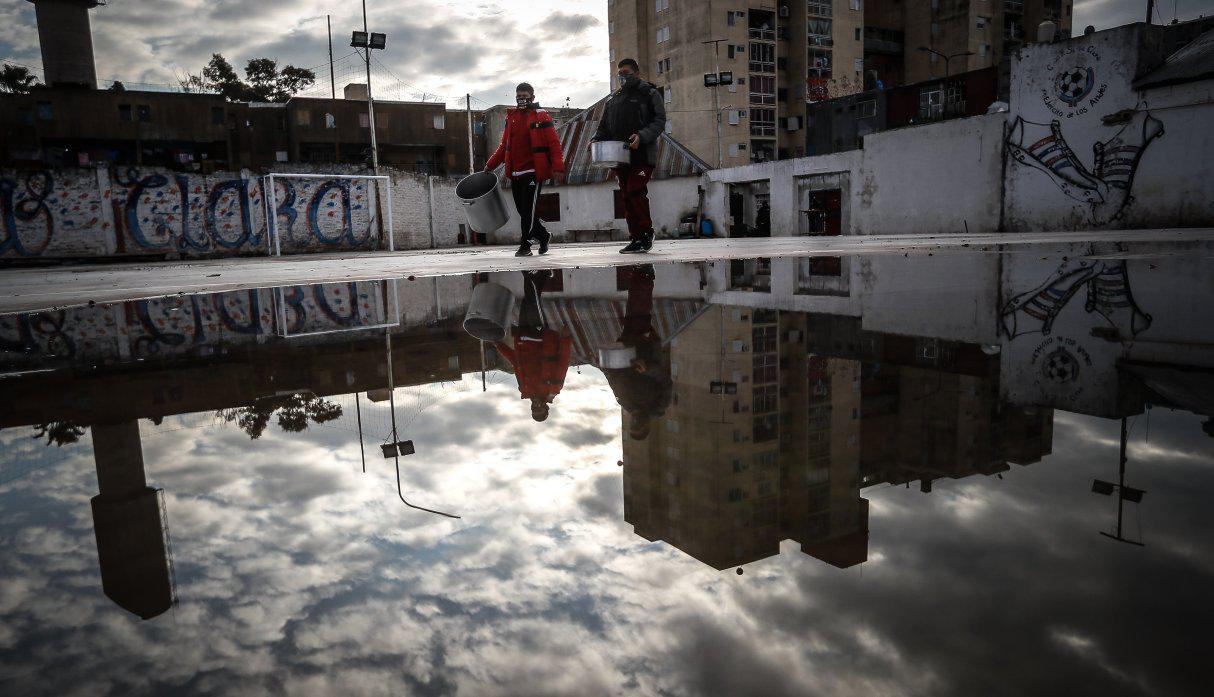 Dos personas caminan con ollas para una comida popular en el barrio Fuerte Apache, provincia de Buenos Aires (Argentina). (EFE/Juan Ignacio Roncoroni).