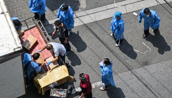 Trabajadores con equipo de protección descargan cajas de un camión a un carro en una calle durante un bloqueo por coronavirus Covid-19 en el distrito de Jing'an en Shanghái el 16 de mayo de 2022. (Foto de Hector RETAMAL / AFP)