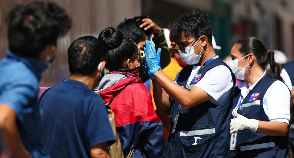 Los trabajadores de salud de Chile verifican la temperatura a las personas que se ubican en los exteriores del consulado peruano en la ciudad de Arica, el 23 de marzo de 2020. (AFP).