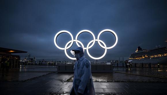 Un hombre pasa junto a los Anillos Olímpicos iluminados al anochecer en Yokohama, el 2 de julio de 2021. (Philip FONG / AFP).