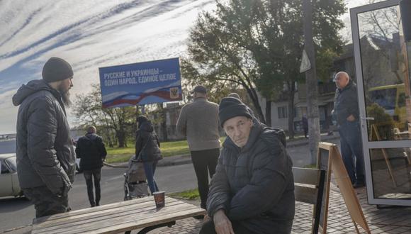 El hombre bebe su café con una cartelera del período de ocupación rusa "Los rusos y los ucranianos son un pueblo, un todo" en el fondo mientras la gente regresa a su vida cotidiana en el Kherson recién liberado el 14 de noviembre de 2022, en medio de la invasión rusa de Ucrania. (Foto de BULENT KILIC / AFP)