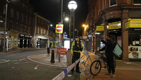 Un repartidos de Deliveroo habla con un oficial de policía que asegura un cordón policial en el centro de Reading, al oeste de Londres, donde ocurrió el mortal ataque. (Adrian DENNIS / AFP)