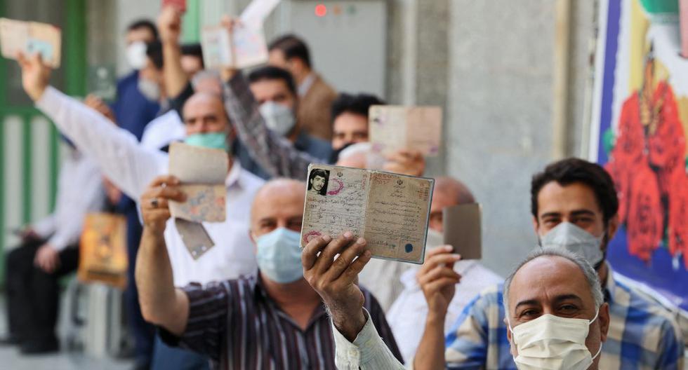 Los hombres iraníes muestran sus identificaciones mientras hacen cola para votar para las elecciones presidenciales en un colegio electoral en Teherán, el 18 de junio de 2021. (ATTA KENARE / AFP).