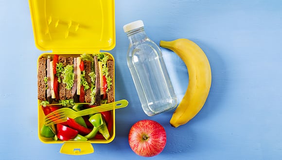 Healthy school lunch box with beef sandwich and fresh vegetables, bottle of water and fruits on blue background. Top view. Flat lay