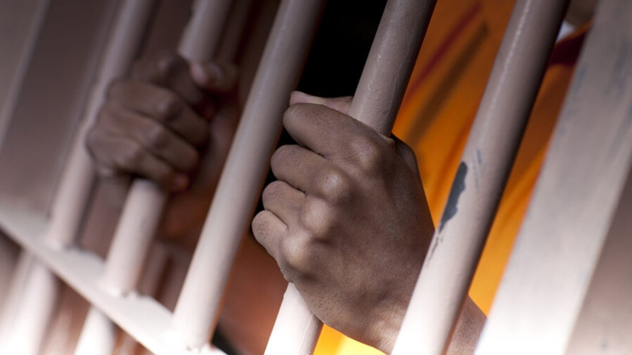 A black man with hands outside the bars of a prison cell