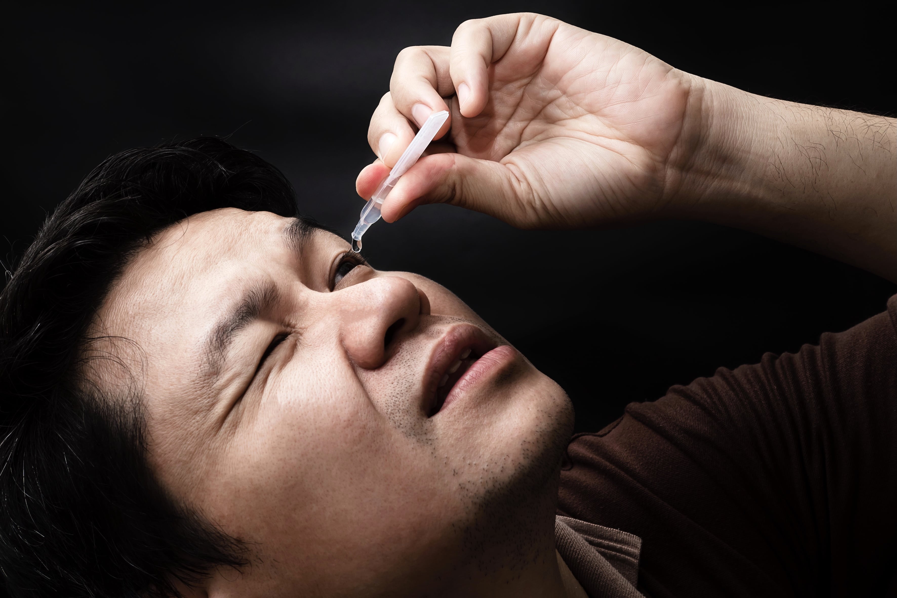 Man dropping eye drop medicine healing his eye pain with black background - health care eye medicine with people concept