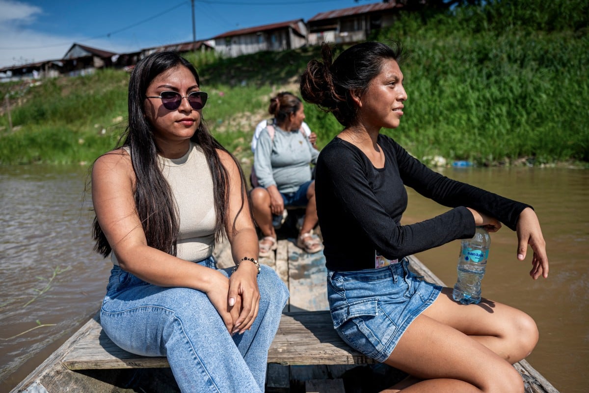 Ketsi Yahuarcani (L) and Wendy Sangama travel in a boat in the Belen district of Iquitos, in the Loreto department in northern Peru, on September 22, 2026. In a misty mountain village in Japan, residents recently welcomed unlikely guests from a Peruvian district along the Amazon River, seeing a chance to revive an ageing community facing extinction. Nanmoku village officials hope a sister-city agreement, which promotes cultural and people-to-people ties, will ultimately attract young people from Belen to live in Nanmoku, although how they might obtain residency remains unclear. (Photo by Junior RABORG / AFP) / To go with AFP story Japan-Peru-social-population-demographics, FOCUS by Natsuko Fukue and Junior Raborg