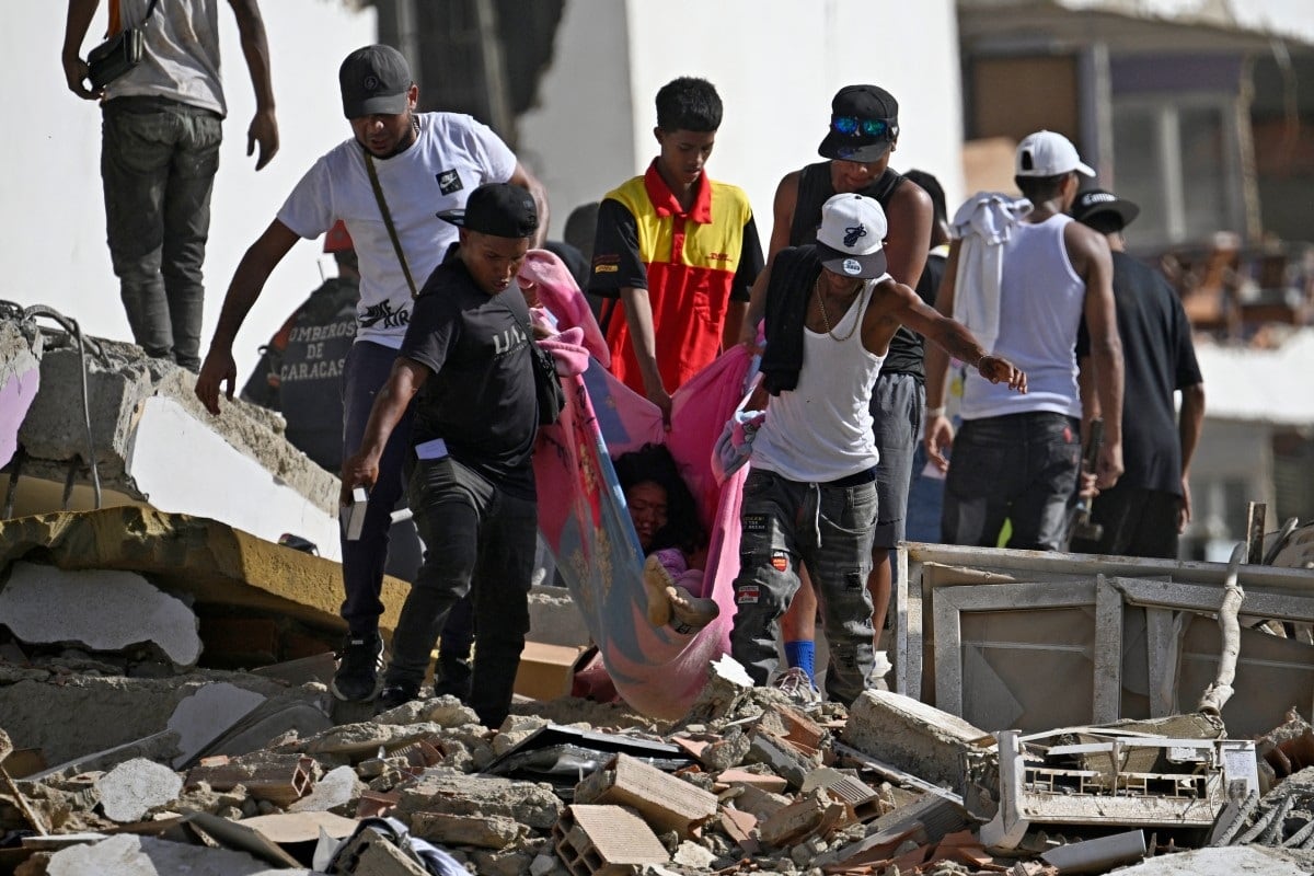 Varias personas transportan a una mujer sobre una manta entre los escombros de un edificio de apartamentos dañado tras un terremoto en Catia La Mar, estado de La Guaira, el 25 de junio de 2026. (Federico PARRA / AFP)