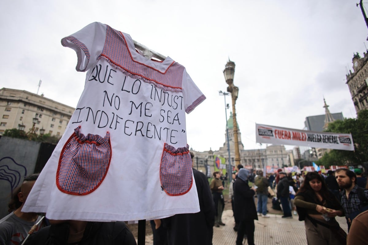 A demonstrator carries a school smock bearing the message "May injustice not leave me indifferent" during a protest by students, lecturers and university workers demanding that the government of Argentine President Javier Milei comply with a law updating funding for public universities, in Buenos Aires on October 15, 2026. (Photo by Emiliano Lasalvia / AFP)