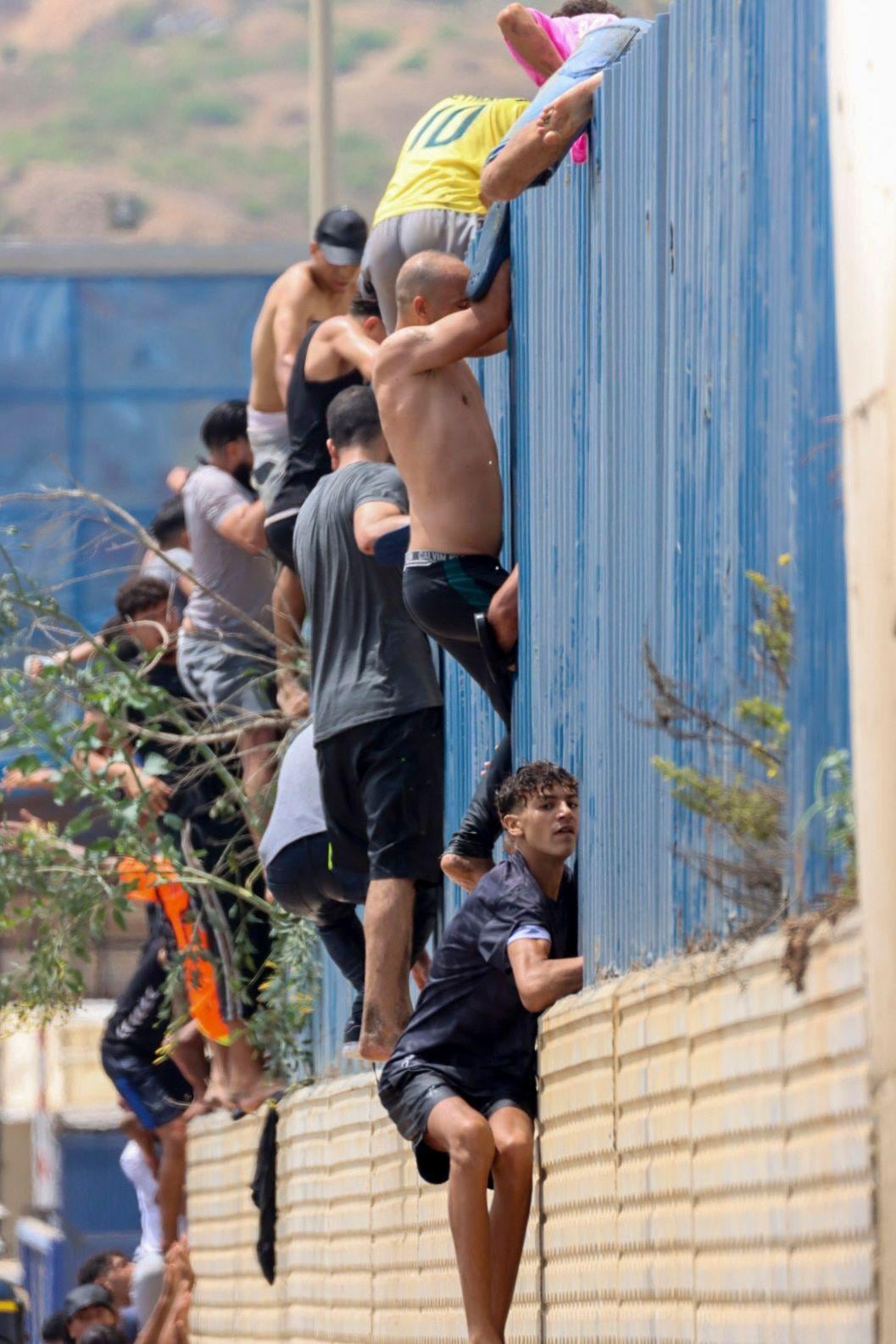 Migrantes trepan una valla en territorio español tras nadar desde Marruecos hasta Ceuta.