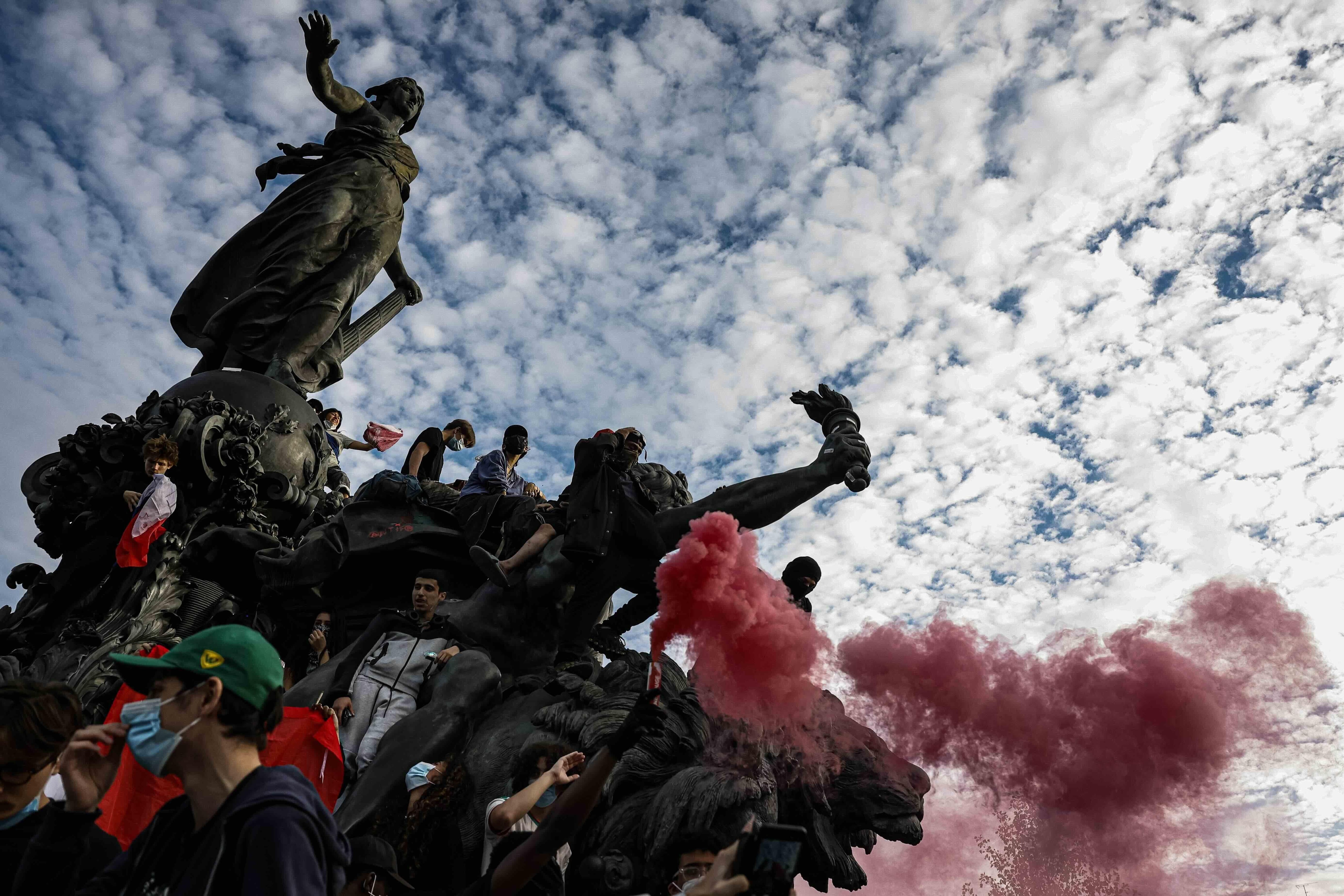 Estudiantes congregados en una estatua en Francia con una bengala que lanza humo rojo