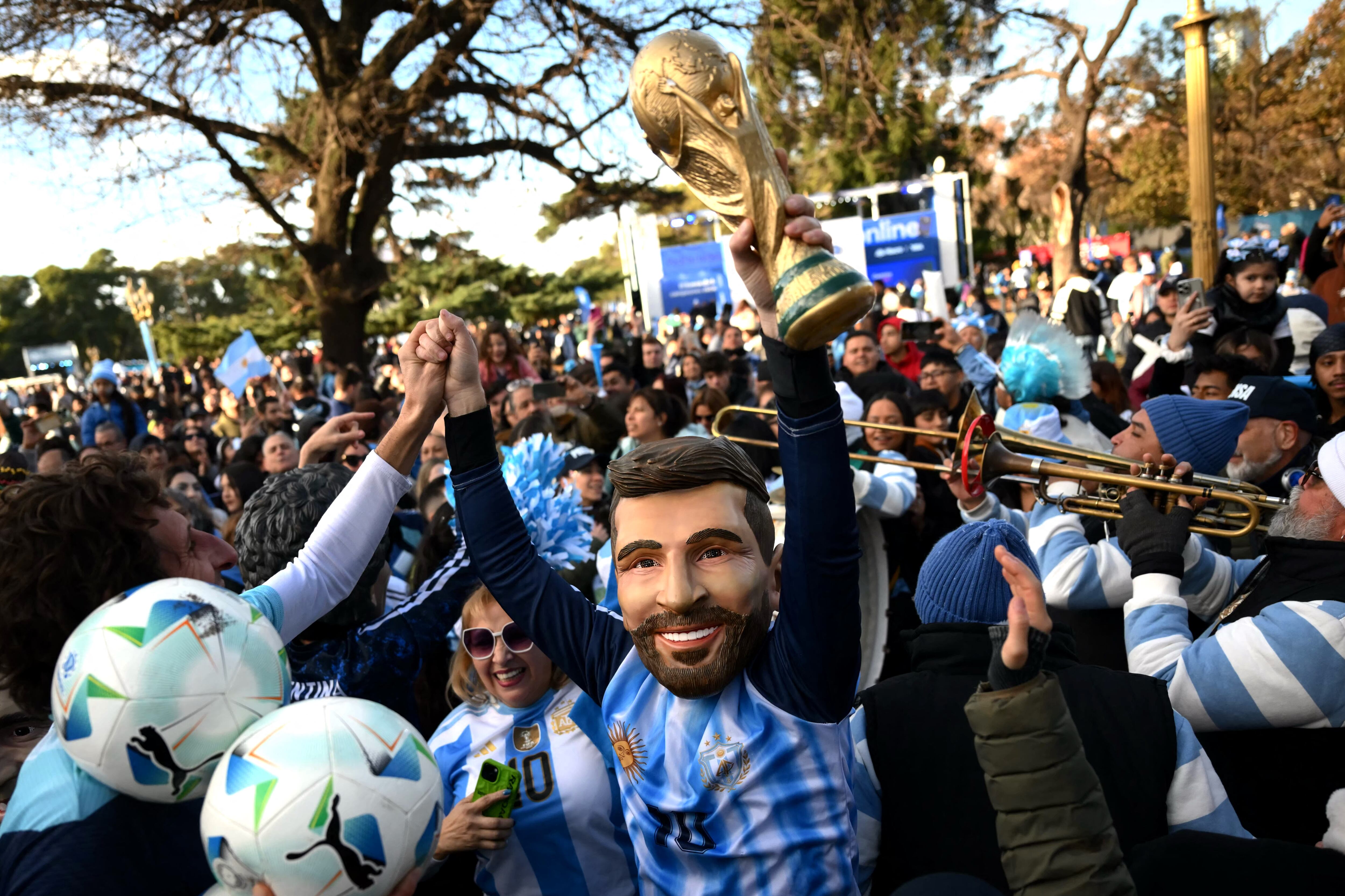 An Argentina fan wearing a mask of Argentine forward Lionel Messi celebrates while raising a replica of the FIFA World Cup trophy following the 2026 FIFA World Cup football match between Argentina and Austria in Buenos Aires on June 22, 2026. (Photo by Luis ROBAYO / AFP)