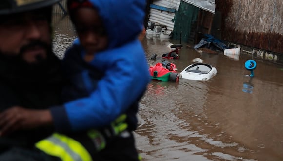 Bomberos evacuan a vecinos de una favela ubicada a orillas del río Mapocho, pues el río se desbordaría por las fuertes lluvias en la comuna de Talagante, Santiago, el 13 de junio de 2024. (Foto de Javier TORRES / AFP)