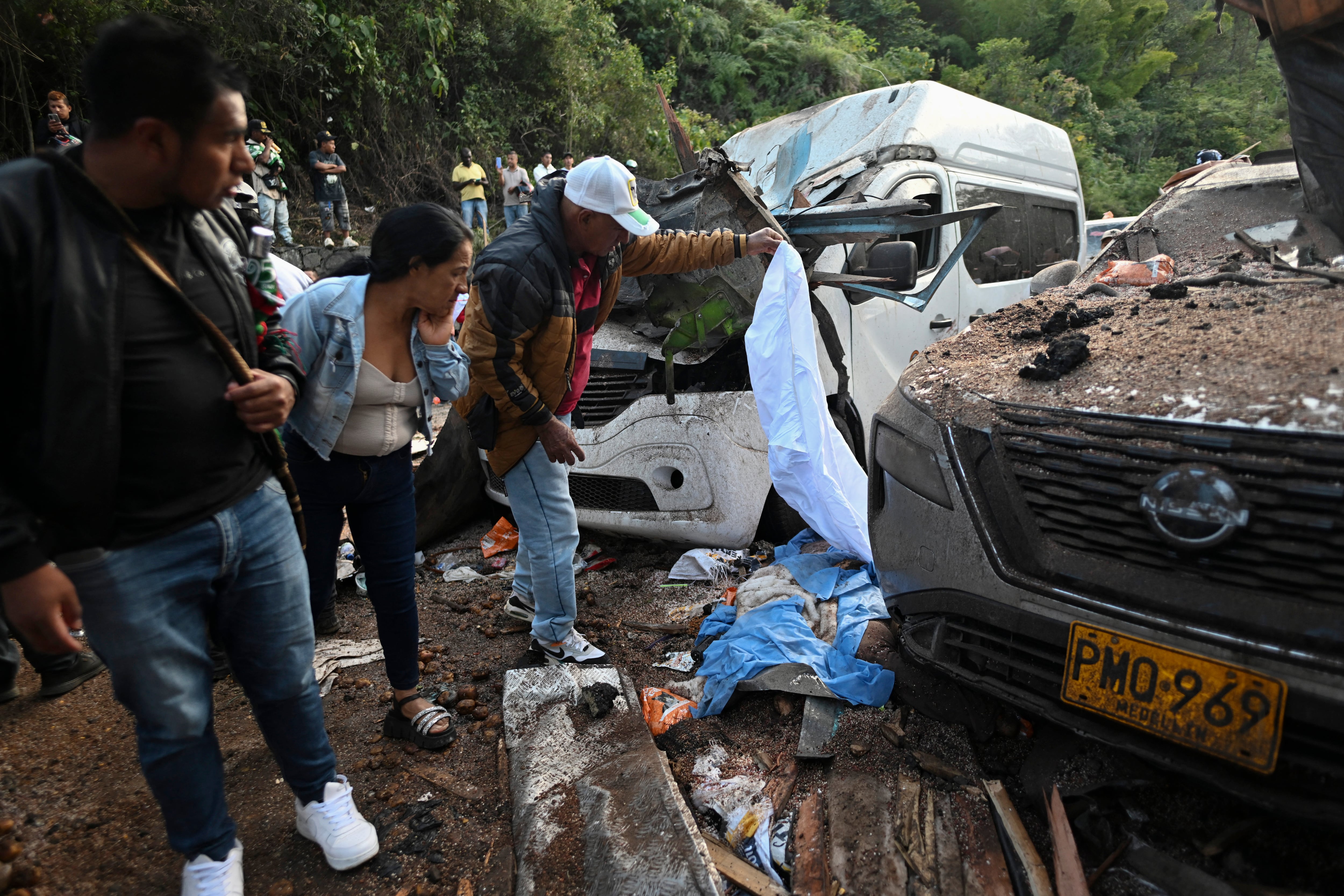 EDITORS NOTE: Graphic content / People stand next to the body of one of the victims, covered with a blue sheet, after a bomb attack at El Tunel, on the Popayan-Cali road, in Cajibio, Cauca department, Colombia, on April 25, 2026. A bomb attack on April 25 left seven people dead and 20 injured in an area of Colombia with a strong guerrilla presence, amid a spate of attacks just over a month before the presidential elections, the governor of the Cauca region said. (Photo by JOAQUIN SARMIENTO / AFP)