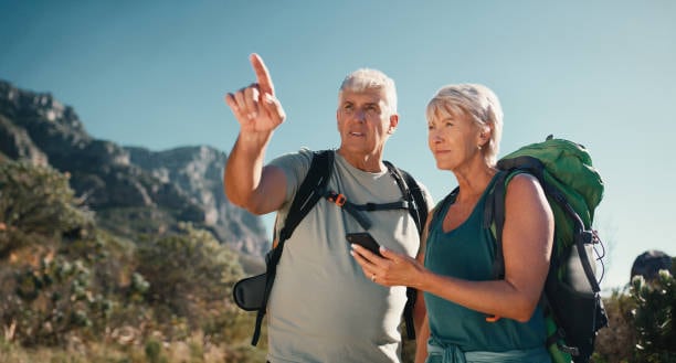 Senior couple, phone map and outdoor with hiking for navigation, direction with app on walk in nature. Location search, lost and web check with conversation and mountain with health