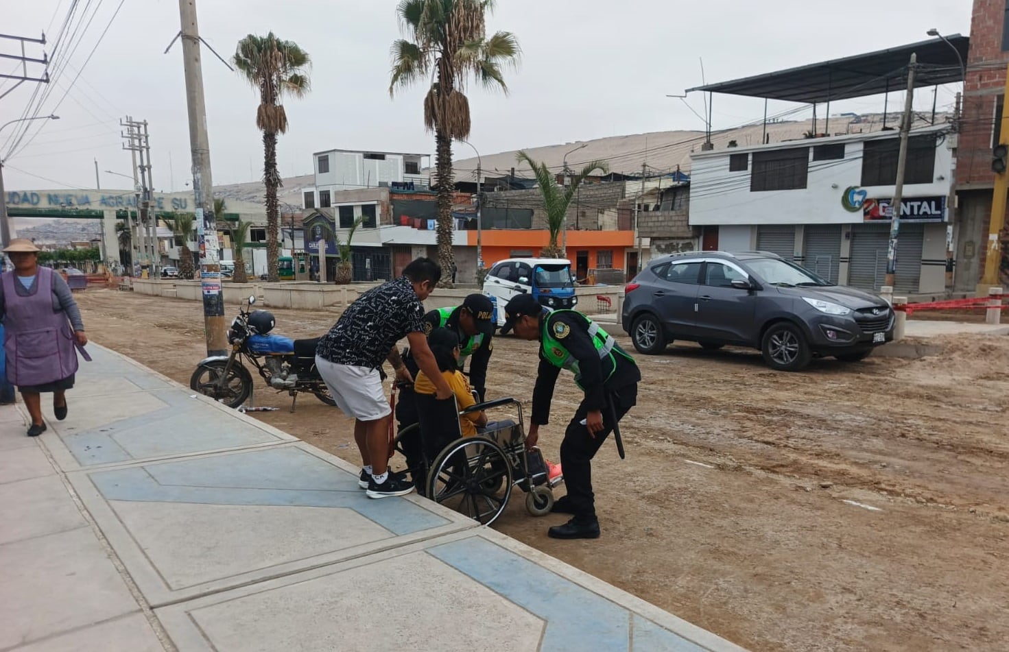 Policías ayudan a hombre en silla de ruedas cruzar la avenida Internacional en refacción para llegar a la puerta de IE Cáceres