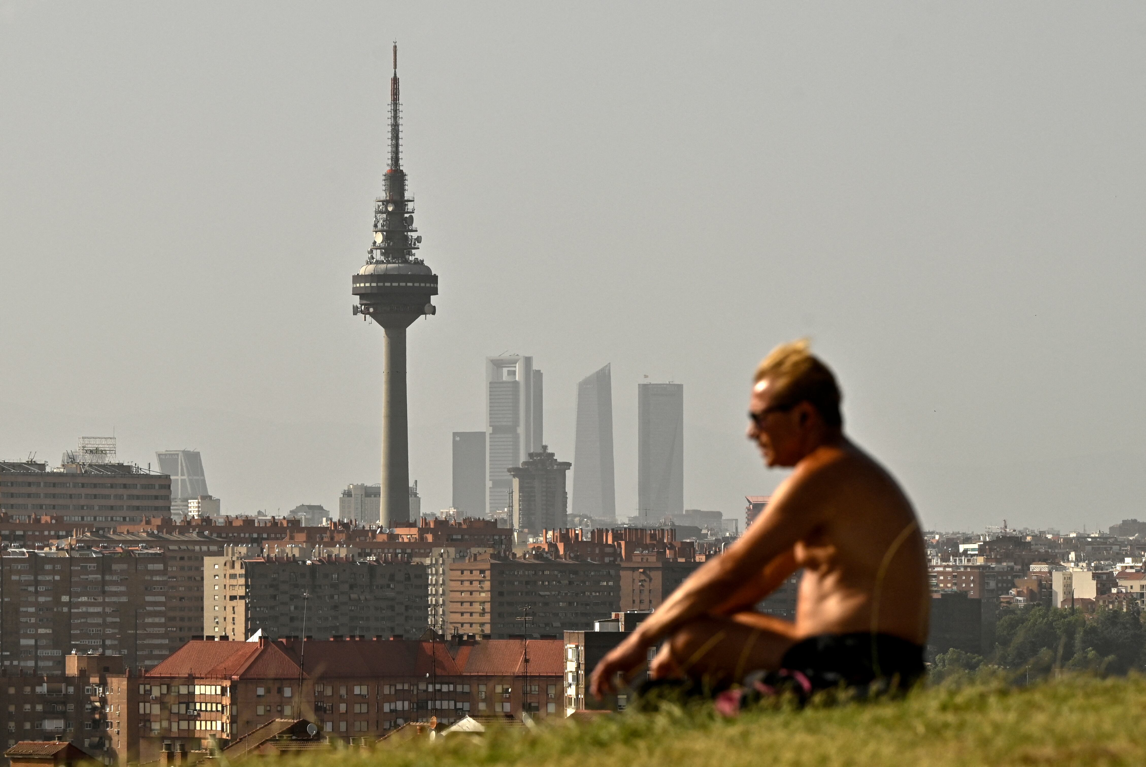 Un hombre se sienta en un parque con el horizonte de Madrid de fondo en medio de partículas que transportan neblina, un fenómeno conocido como 'Kalima' ('Calima') durante una ola de calor en Madrid el 19 de julio de 2023. (Foto por ÓSCAR DEL POZO / AFP)