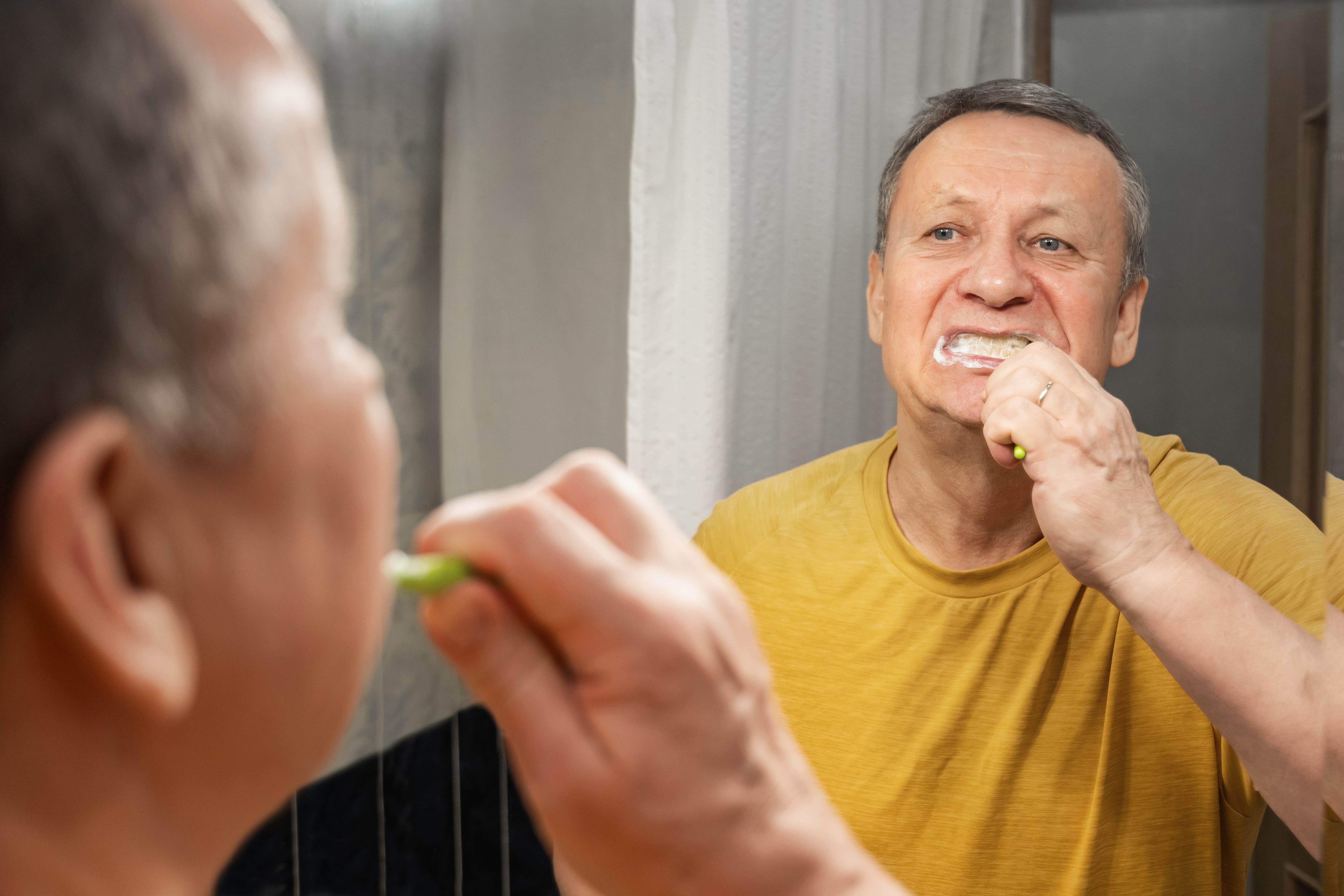 Brushing teeth with foam in mirror, caucasian adult male performing morning oral hygiene routine at bathroom sink. Man Brushing Teeth