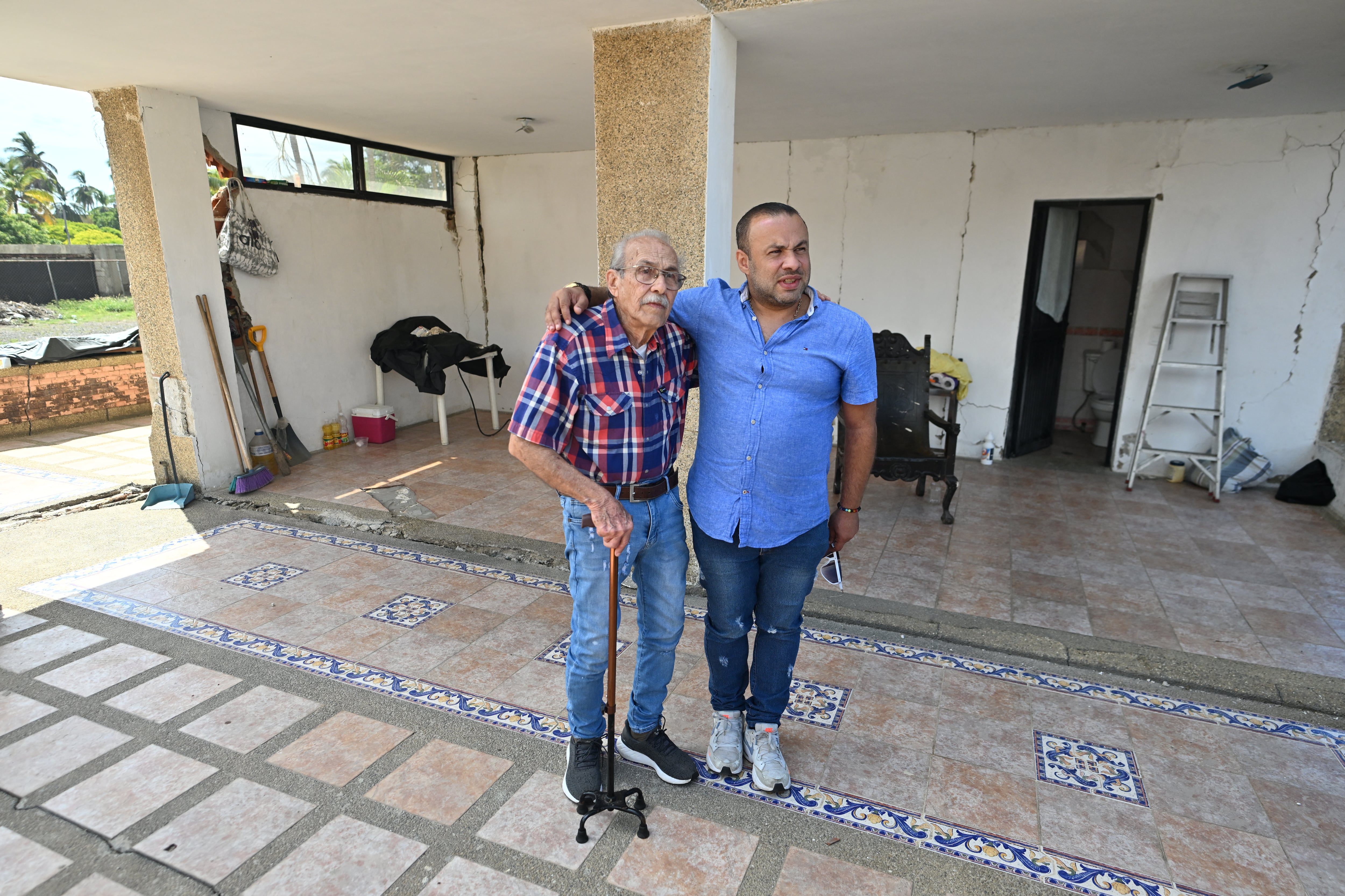 Engineer Elias Chayeb (L) and his son, engineer Elias Eduardo Chayeb, pose for a picture in Catia La Mar, La Guaira state, Venezuela, on July 6, 2026. In a block of flats reduced to ruins, a modest three-storey building still stands. The engineer who helped build it wept with joy when he saw that it had withstood the two violent earthquakes that left more than 3,500 people dead in Venezuela. (Photo by Juan BARRETO / AFP)