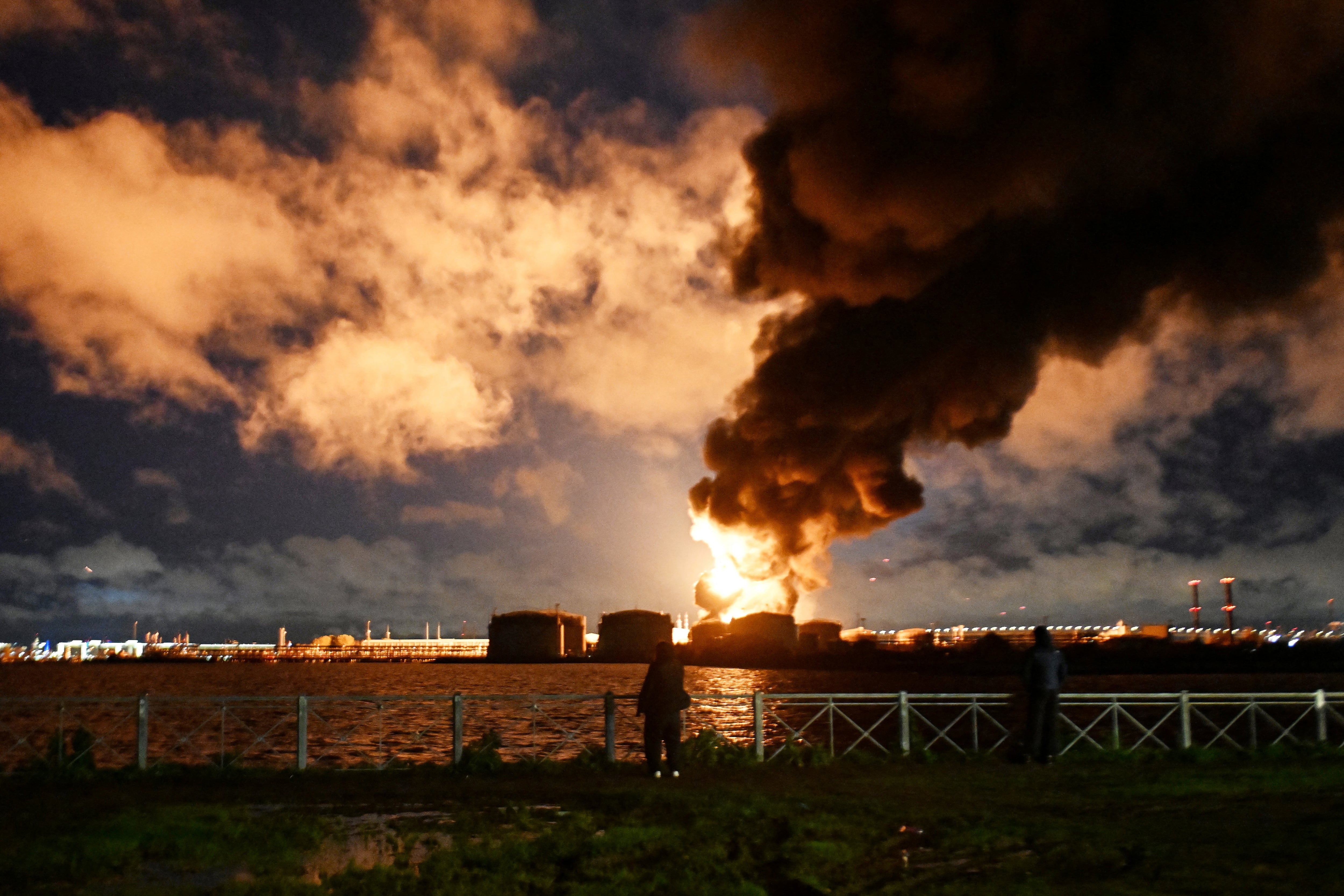 Varias personas observan la terminal petrolera en llamas tras un ataque aéreo en San Petersburgo el 18 de octubre de 2026, en medio del conflicto ruso-ucraniano. (Foto: AFP).
