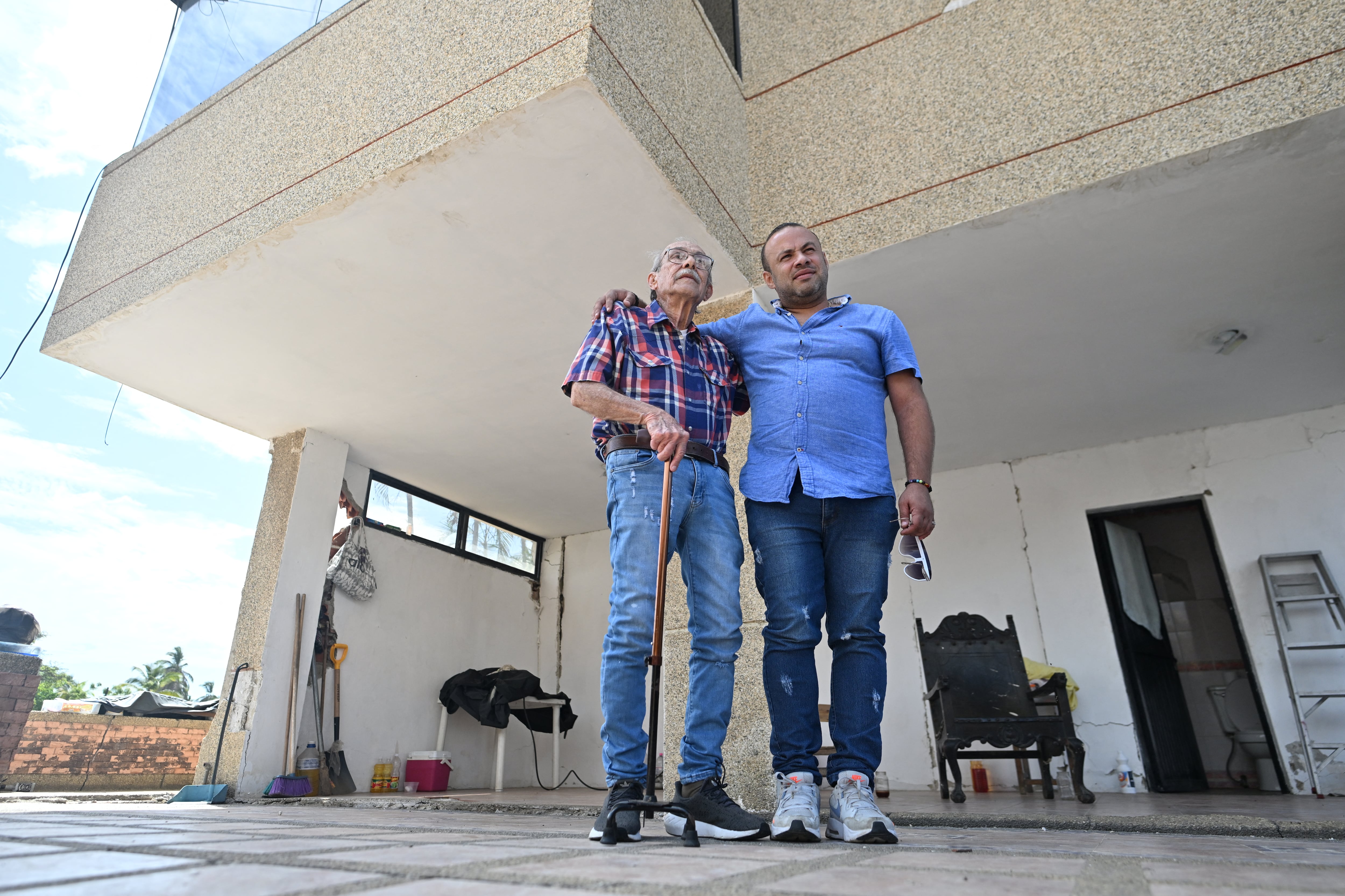 Engineer Elias Chayeb (L) and his son, engineer Elias Eduardo Chayeb, pose for a picture in Catia La Mar, La Guaira state, Venezuela, on July 6, 2026. In a block of flats reduced to ruins, a modest three-storey building still stands. The engineer who helped build it wept with joy when he saw that it had withstood the two violent earthquakes that left more than 3,500 people dead in Venezuela. (Photo by Juan BARRETO / AFP)