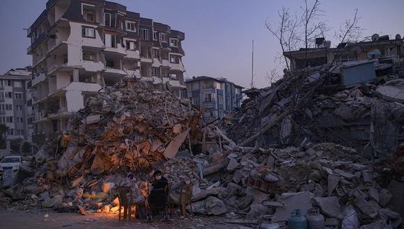 Las personas se sientan junto a una fogata cerca de los edificios derrumbados en Hatay el 13 de febrero de 2023, mientras los equipos de rescate comenzaron a reducir la búsqueda de sobrevivientes. (Foto de Yasin AKGUL / AFP)