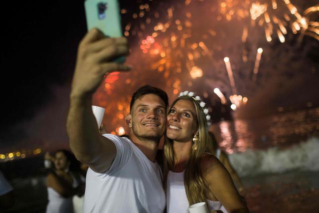 A couple takes a selfir in front of the traditional New Year's fireworks at Copacabana Beach in Rio de Janeiro, Brazil, on December 31, 2019.  / AFP / DANIEL RAMALHO