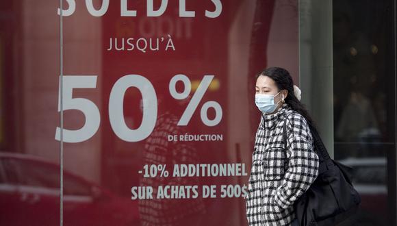 Una mujer usa una mascarilla mientras pasa por un escaparate con descuentos de venta publicitaria en el Boxing Day en Montreal. (Graham Hughes / The Canadian Press vía AP)