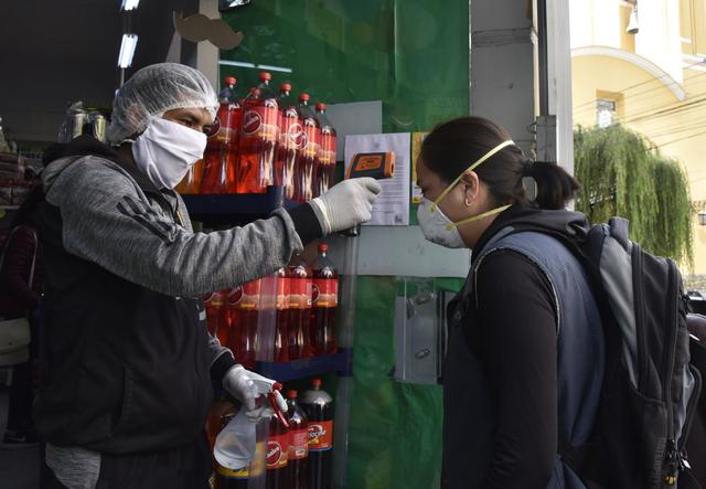 Un trabajador verifica la temperatura de un cliente en una entrada al mercado como medida preventiva contra la propagación del nuevo coronavirus, COVID-19, en un mercado en La Paz, Bolivia. (Foto: AFP)