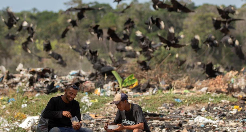 Venezolanos son vistos en el basurero municipal comiendo y en el fondo una bandada de buitres los acechan hoy viernes en la ciudad de Pacaraima, Brasil. (EFE)